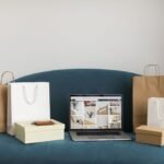 A laptop surrounded by shopping bags and boxes on a blue sofa, ideal for online shopping themes.