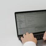 Hands typing code on a laptop in a workspace. Indoor setting focused on software development.
