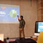 Young man delivering a business presentation on ad spend with charts and graphs in a modern office setting.