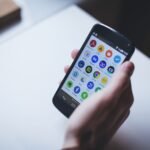 Close-up of a person holding a smartphone with various app icons visible on the screen.