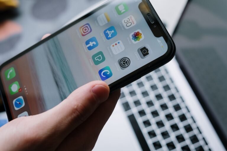 Person holding a smartphone in front of a laptop showcasing various app icons, highlighting digital connectivity.