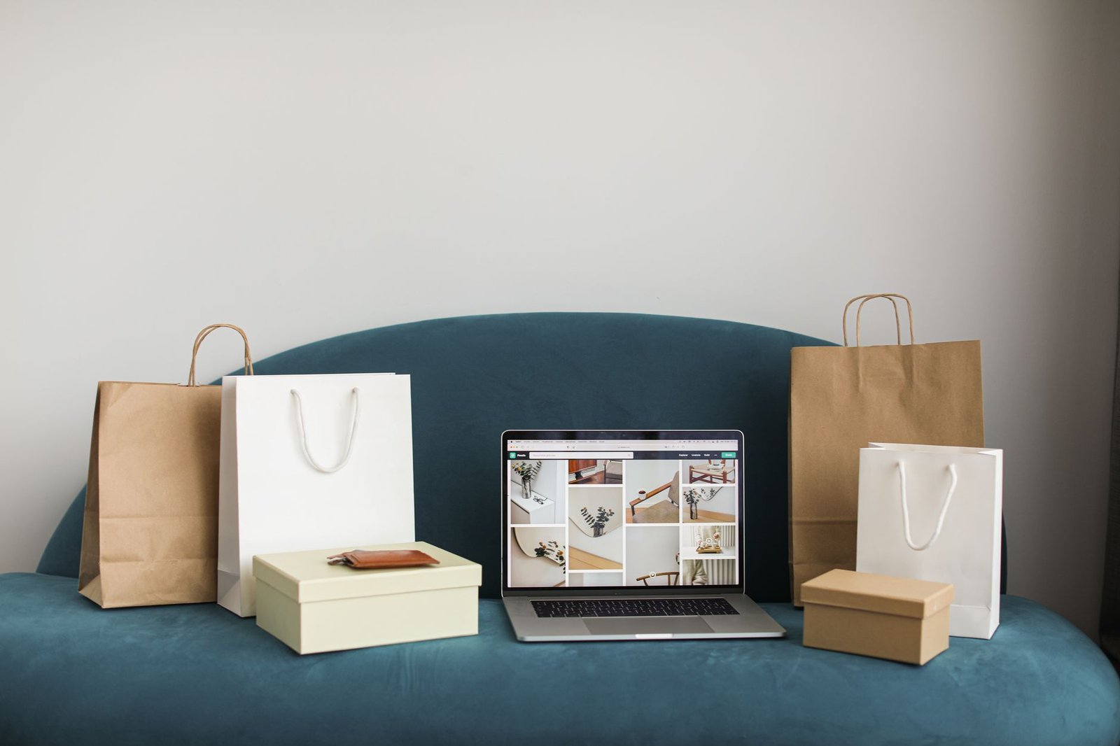 A laptop surrounded by shopping bags and boxes on a blue sofa, ideal for online shopping themes.