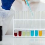 Scientist in protective gear using a dropper to fill test tubes with colorful liquids in a laboratory.