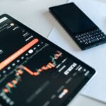 Close-up of a tablet displaying financial graphs, a smartphone, and a pen on a table.