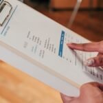 Close-up image of a person pointing to a document on a clipboard, indoors.