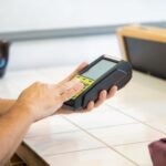 Close-up of hands using a POS machine in a retail setting, emphasizing digital payment.