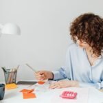 Woman in office calculating expenses with documents, calculator, and coffee.