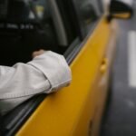 Unrecognizable man in shirt and eyeglasses sitting in yellow cab while looking away in soft daylight