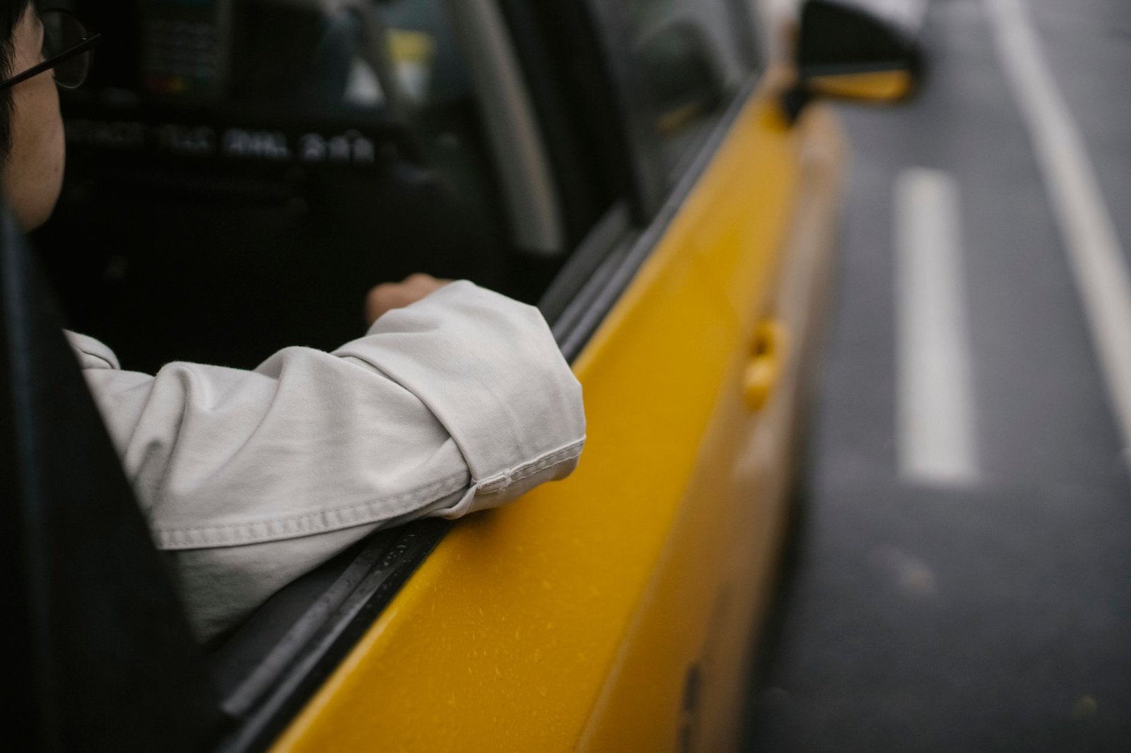 Unrecognizable man in shirt and eyeglasses sitting in yellow cab while looking away in soft daylight