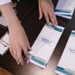 Hands organizing conference programs and name tags at event registration desk.
