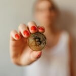 Focused shot of a Bitcoin coin held by a person with red nails, symbolizing digital currency.