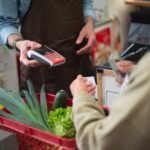 Close-up of customer paying for groceries with produce at a store checkout counter.
