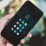 Close-up of a hand holding a smartphone with app icons and a nature wallpaper.