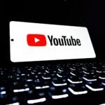 YouTube app icon displayed on a smartphone over an illuminated keyboard, representing digital media and online streaming.