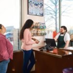 Two customers interacting with staff at a restaurant point of sale counter.