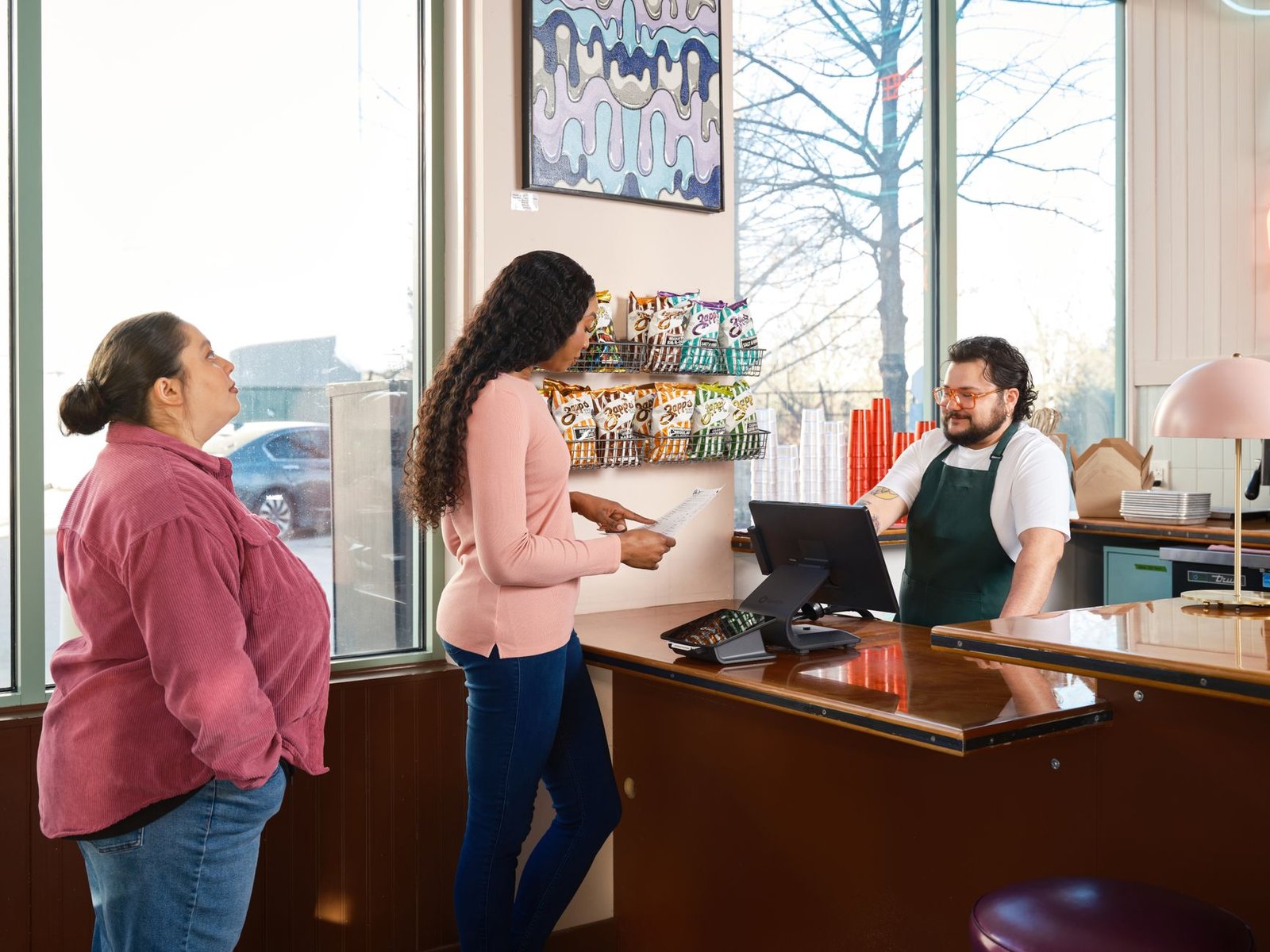 Two customers interacting with staff at a restaurant point of sale counter.
