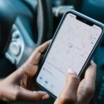 Close-up of hands holding a smartphone with GPS navigation displayed, in a car setting.