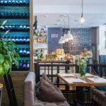 Through glass of contemporary restaurant with soft furniture and various decorative elements on shelves
