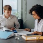 Two business colleagues analyzing financial reports at a desk in a modern office environment.