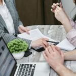 Professional meeting discussing business agreements with laptops and documents on a rustic table.