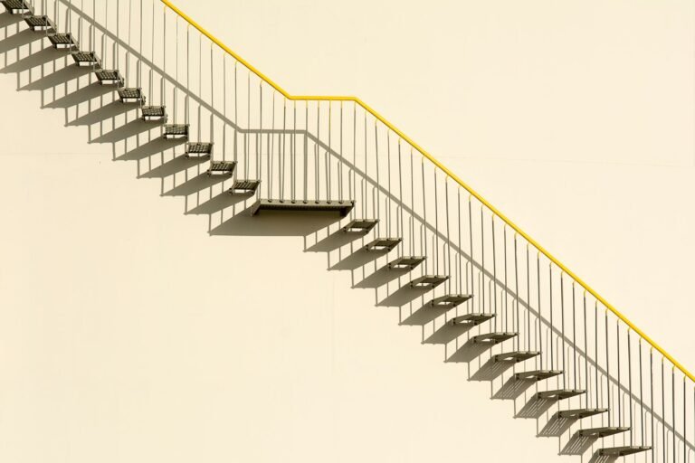 A simple outdoor metal staircase on a concrete wall casting shadows, showcasing minimalistic architecture.