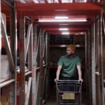 A worker in a warehouse pushing a cart through shelves, depicting concentration and industrial work.