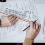An architect uses a ruler and pencil on blueprints, showcasing workspace and planning.